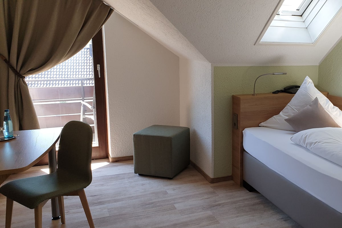 Una habitación de hotel con cama, escritorio, silla y un pequeño reposapiés.