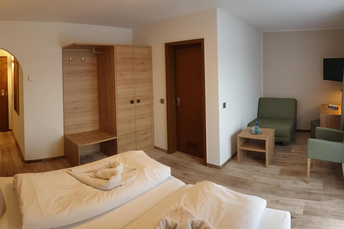 Una habitación de hotel con cama, un armario de madera, un sillón verde, una mesita y un televisor fijado a la pared.