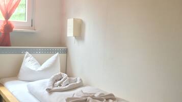 A single bed with white bedding, a window with red curtains, a wall-mounted light, and a framed picture on the wall.