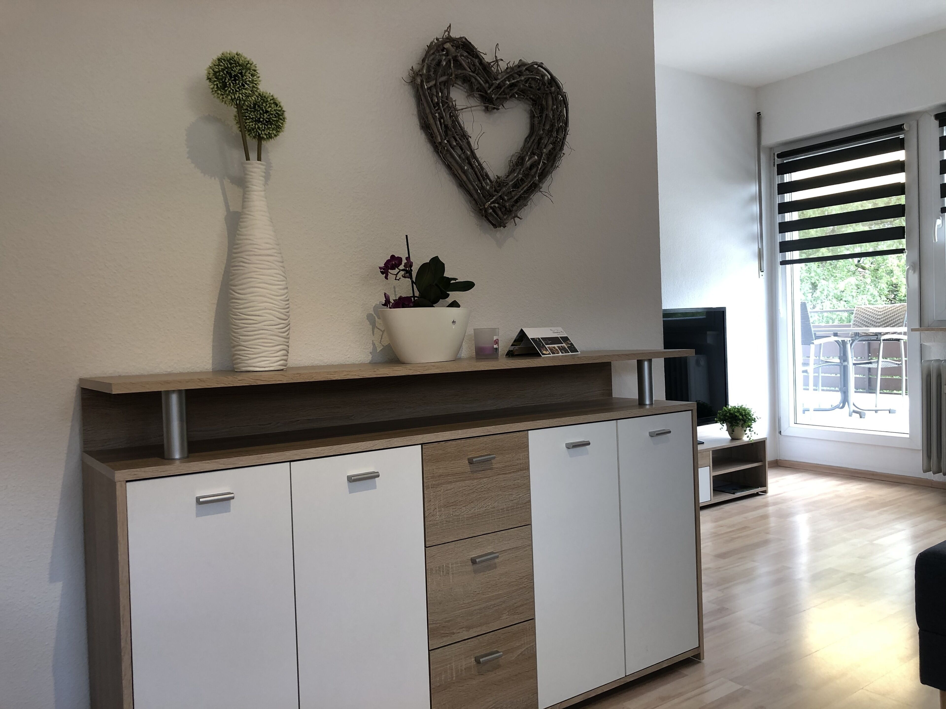 Una sala de estar moderna con un mueble de madera, un adorno de pared con forma de corazón y una planta en maceta.
