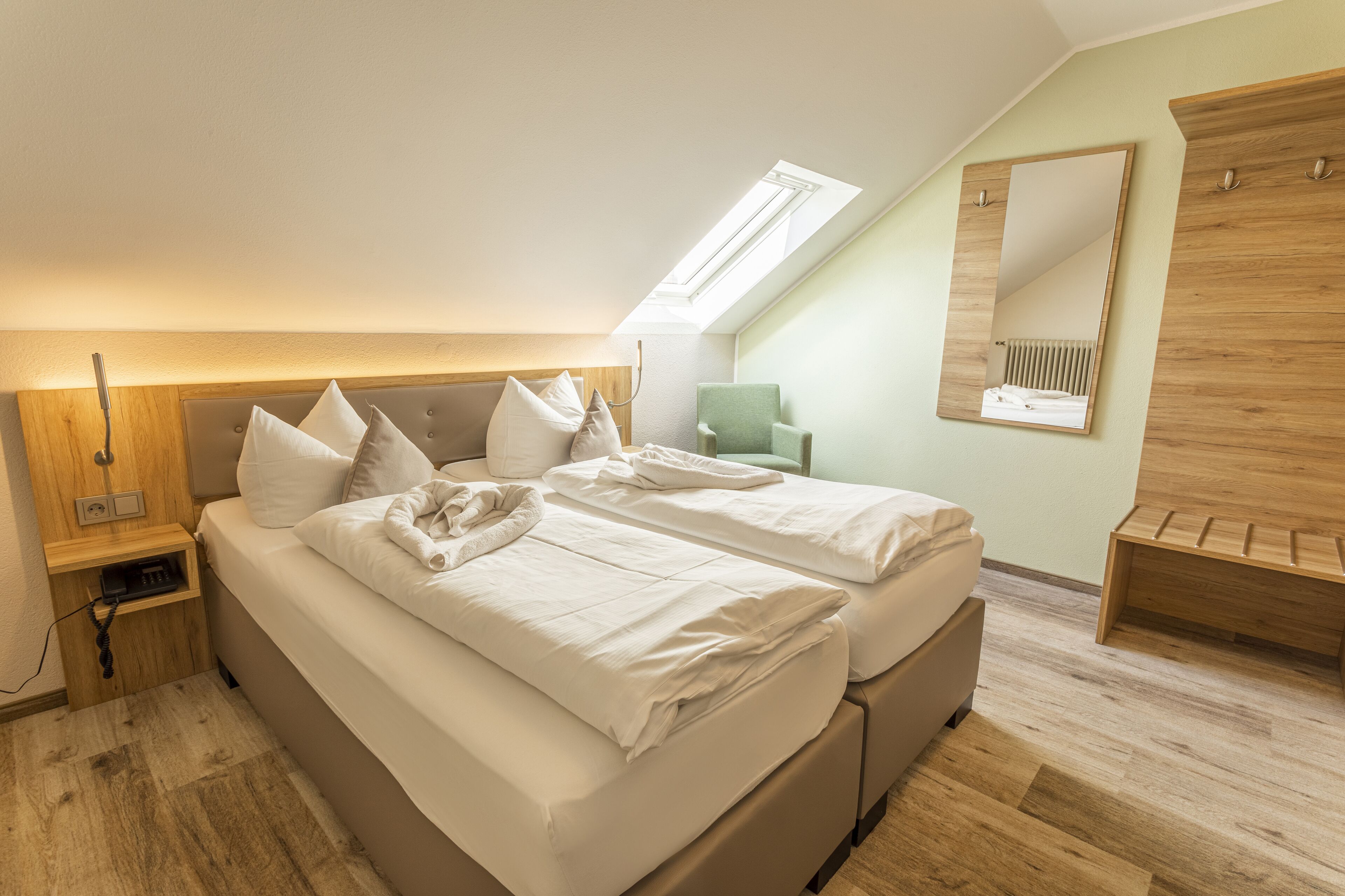 A bedroom with a large bed, a bedside table, a chair, a mirror, and a skylight.