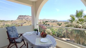Ein Balkon mit Tisch für zwei Personen, mit Blick auf eine malerische Landschaft mit Hügeln und blauem Himmel.