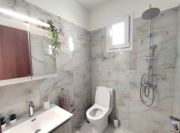 A bathroom with a marble wall, a sink, a toilet, and a shower.