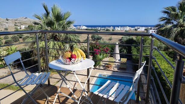 Ein Balkon mit Pool, weißen Liegestühlen und einem Tisch mit Obst.