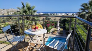 A balcony with a pool, white lounge chairs, and a table with fruit.
