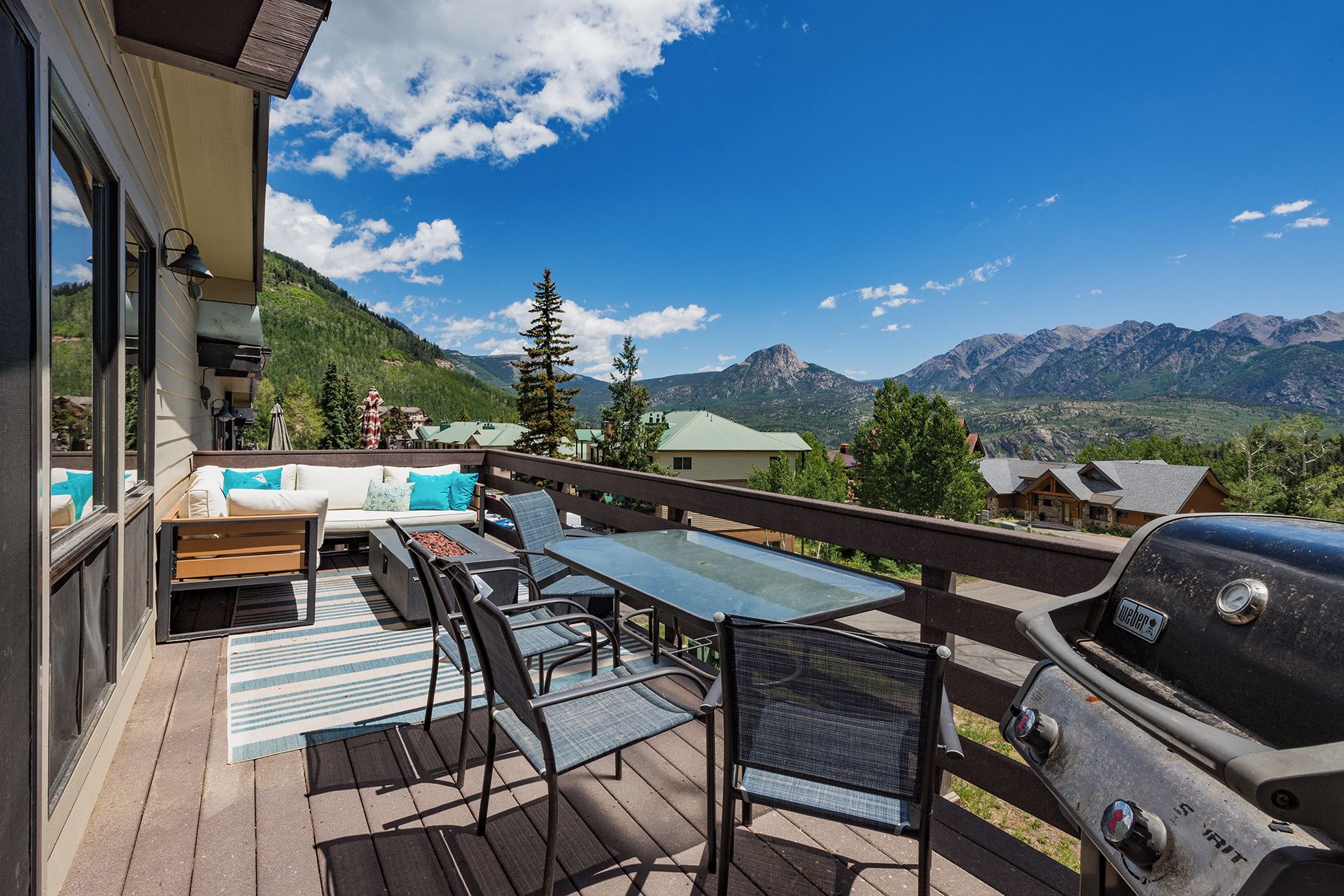 A deck with outdoor furniture, a grill, and a view of mountains.