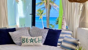 A sofa with multiple pillows, including one with "BEACH" written on it, positioned near a window with a view of palm trees and the ocean. - Affordable, bright studio with beach access, AC and WiFi! (Akumal)