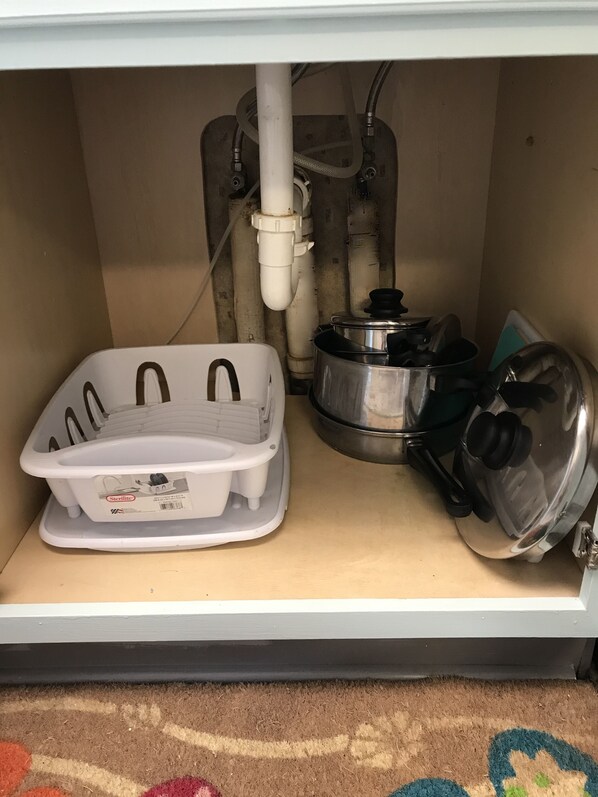 A kitchen with a white sink, a stainless steel pot, and a plastic container.