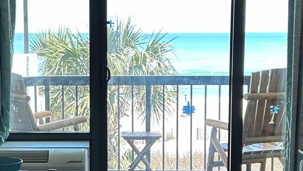 A balcony with a view of the beach and ocean, wooden chairs, and a small table.