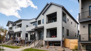 A modern multi-story residential building with a flat roof, large windows, and a covered front porch.