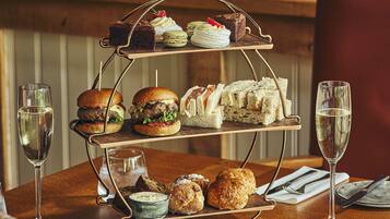 A three-tiered dessert stand with various pastries and sandwiches on a wooden table, accompanied by two glasses of champagne.