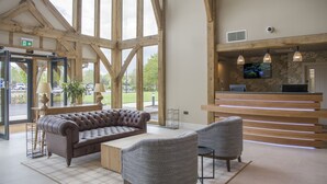 A reception area with a wooden reception desk, a large leather sofa, and two grey armchairs. - Sandburn Hall Hotel (York)