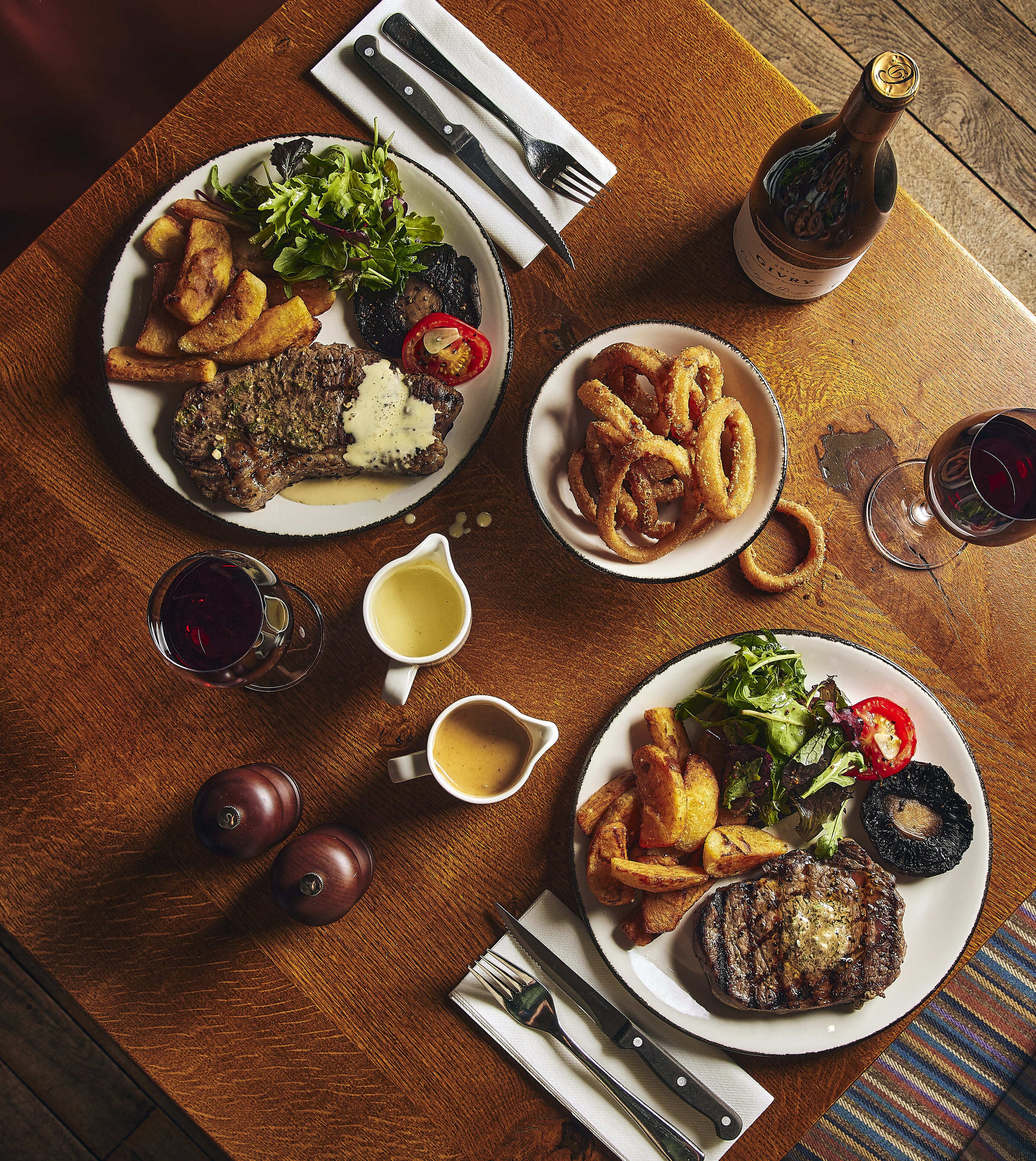 A dining table with plates of food, cutlery, and glasses of wine.