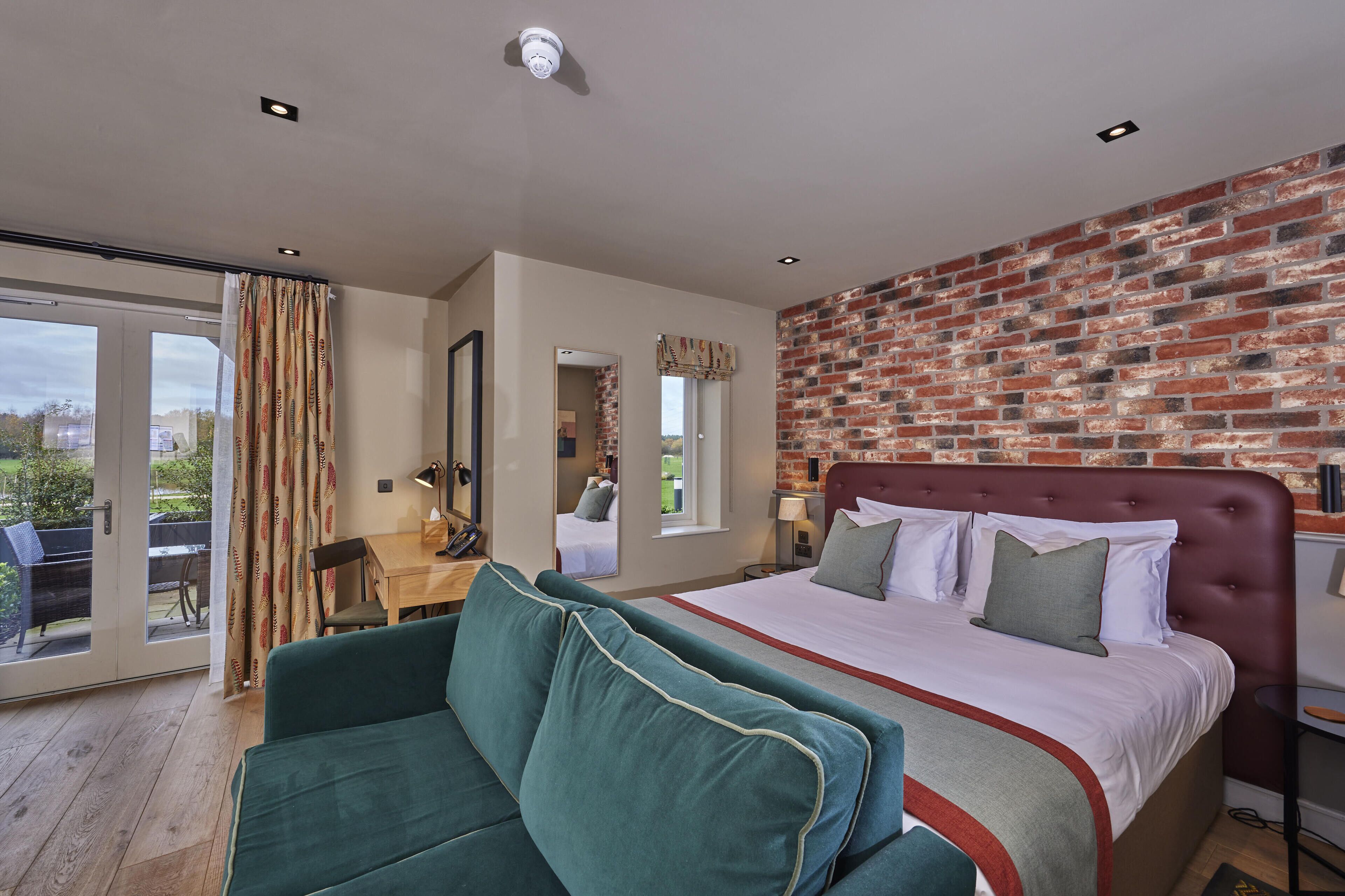 A hotel room with a large bed, a green sofa, a desk, and a brick wall.