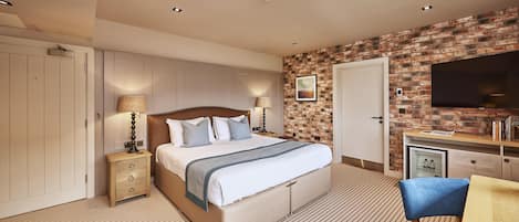 A hotel room with a bed, bedside lamps, a TV, and a brick wall.