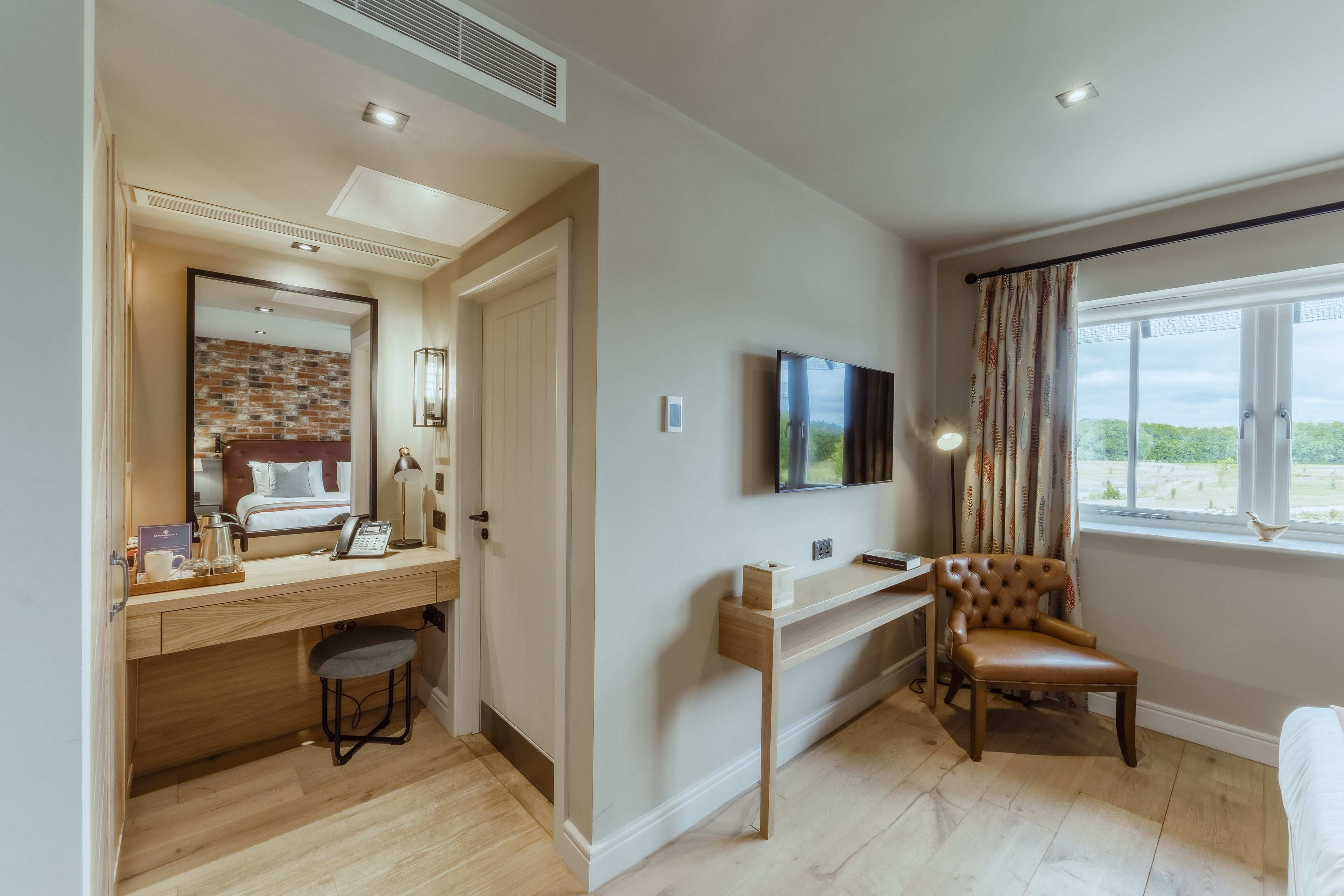 A hotel room with a wooden desk, a comfortable chair, a flat-screen TV, and a large window with curtains.