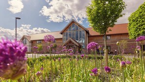A building with a large glass facade, a wooden exterior, and a landscaped garden with purple flowers. - Sandburn Hall Hotel (York)