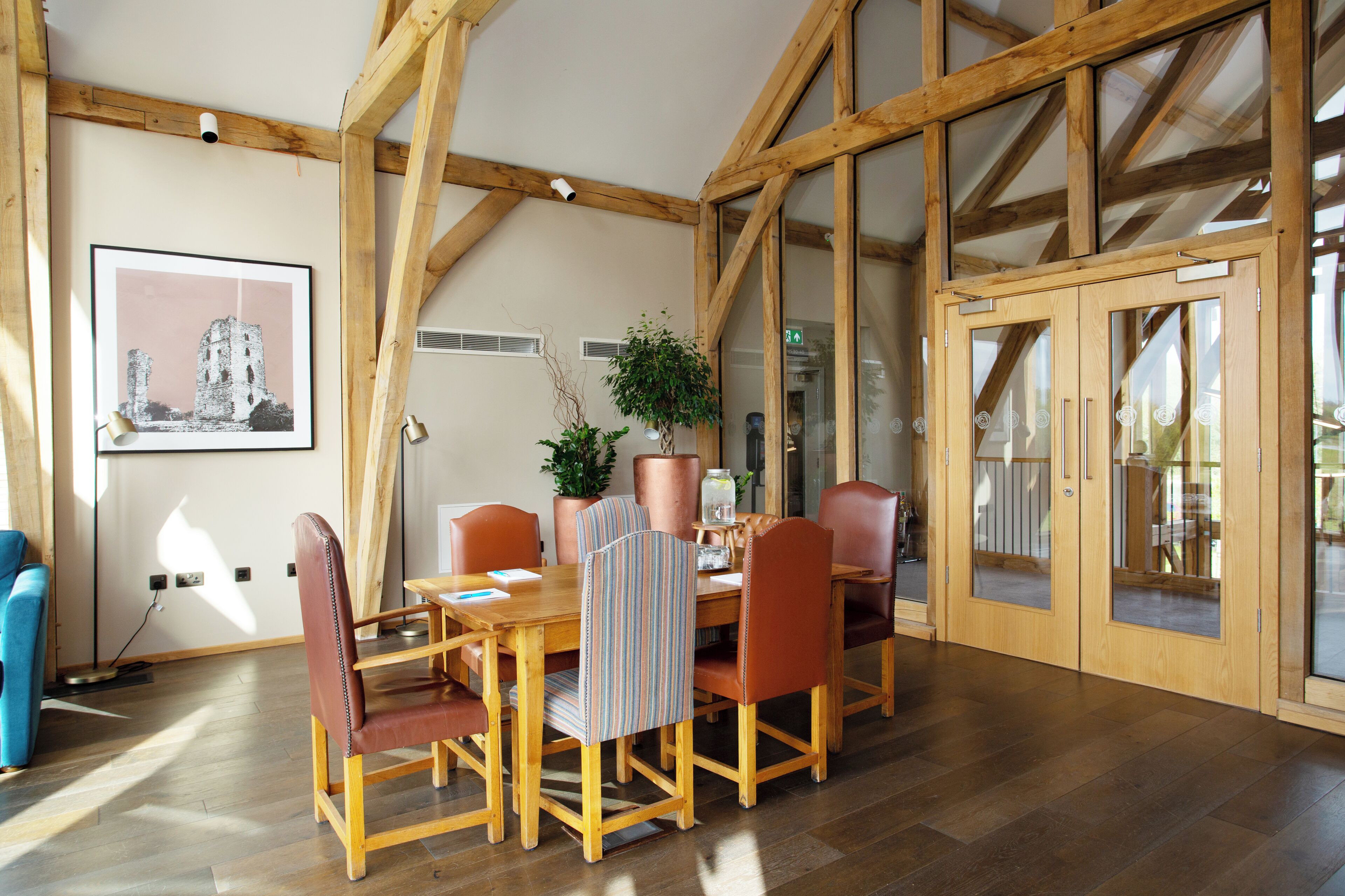 A dining area with wooden beams, a table with chairs, a framed picture on the wall, and a potted plant.