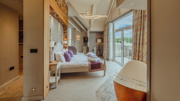 A modern hotel room with a large bed, a sitting area with a chair, a view of the outdoors, and a balcony. - Sandburn Hall Hotel (York)