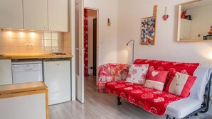 A compact living space with a kitchenette, a red patterned sofa, and a mirror on the wall. - 100m from ski slopes, 5th floor, view ski slopes, balcony, tv, ski locker, 19m², Les Orres (Les Orres)