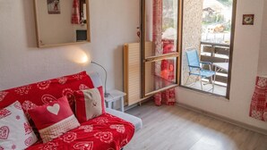 A room with a red patterned sofa, a small table, a mirror, and a sliding glass door leading to an outdoor area with a table and chairs. - 100m from ski slopes, 5th floor, view ski slopes, balcony, tv, ski locker, 19m², Les Orres (Les Orres)