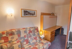 A cozy room with a patterned sofa, a wooden desk, and a wall-mounted shelf. - 100m from resort center, 7th floor, tv, ski locker, 30m², Les Orres (Les Orres)