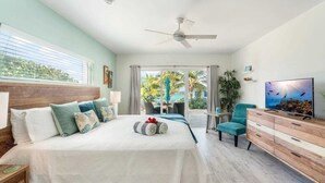 Ein Hotelzimmer mit Bett, Schreibtisch, Stuhl, Fernseher und einem Balkon mit Blick auf Palmen.