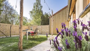Un jardin avec une table et des chaises, une clôture en bois et des plants de lavande.
