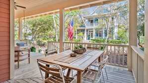 A wooden deck with a table and chairs, overlooking a house with a porch and an American flag. - WaterColor Park District Retreat, 4BR, Bikes & Walk to Beach (Santa Rosa Beach)