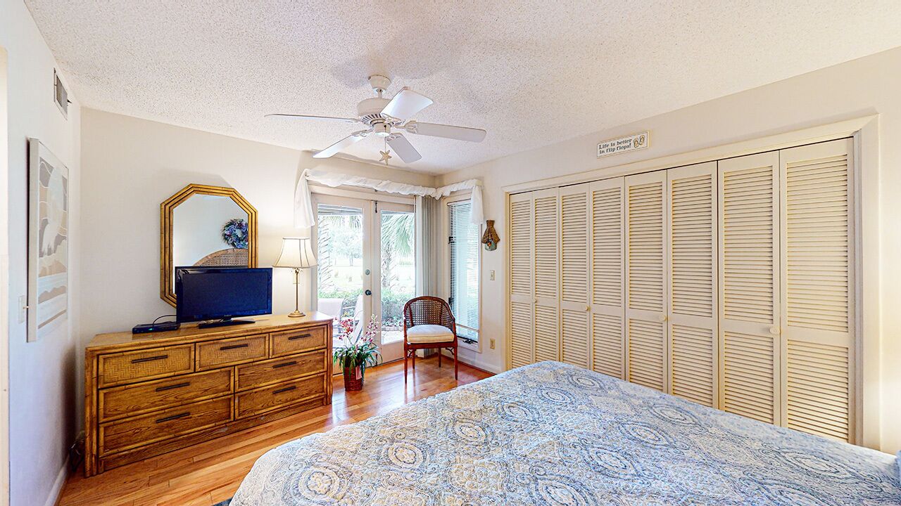 A bedroom with a bed, a dresser, a chair, a ceiling fan, and a closet with louvered doors.