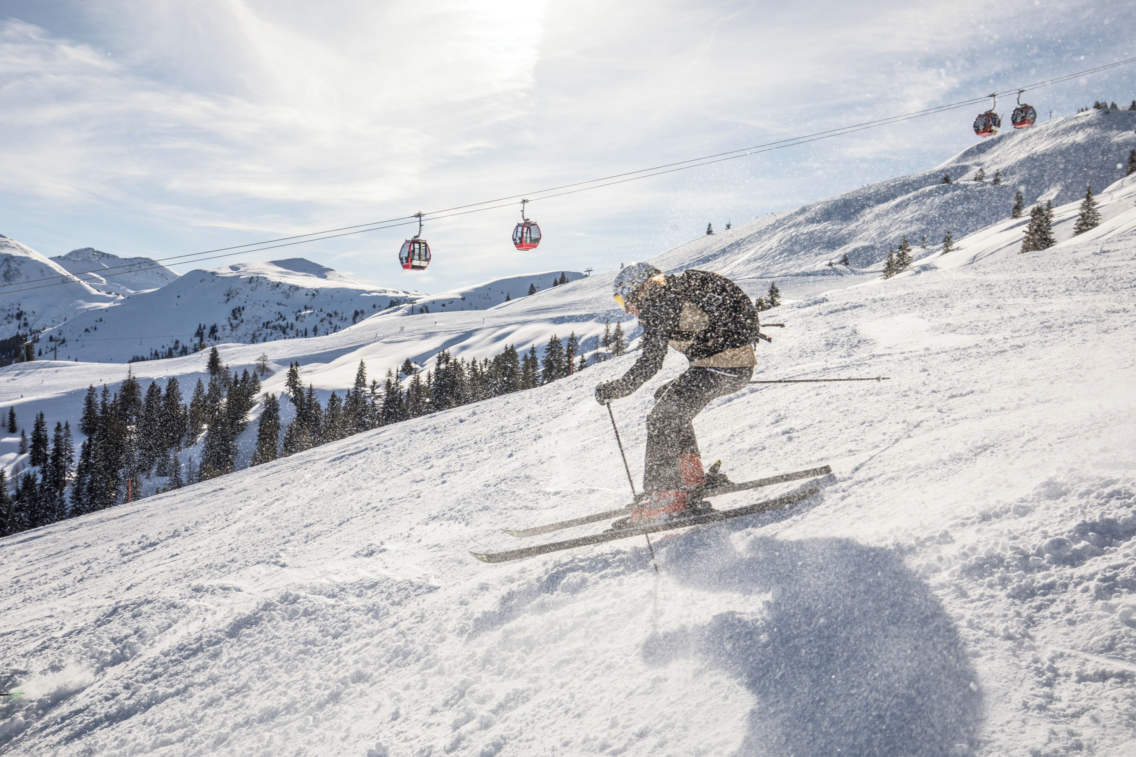 A ski slope with a person skiing down, a ski lift in the background, and snow-covered trees.