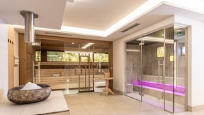 Een modern wellnesscentrum met een houten receptiebalie, een stenen kom, een houten bank en een stoomcabine met glazen wanden en paars licht.