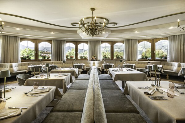 A formal dining room with multiple tables, chairs, and a central bench. - Hotel Pirchnerhof (Reith im Alpbachtal)