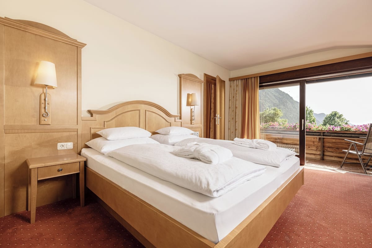 A hotel room with a bed, a nightstand, a lamp, a window with curtains, and a view of the outdoors.