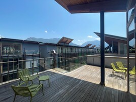 A wooden deck with outdoor seating, glass railings, and a mountain view.