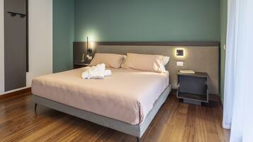 A neatly made bed with a light-colored duvet and pillows, a bedside table with a lamp, and a small shelf unit.
