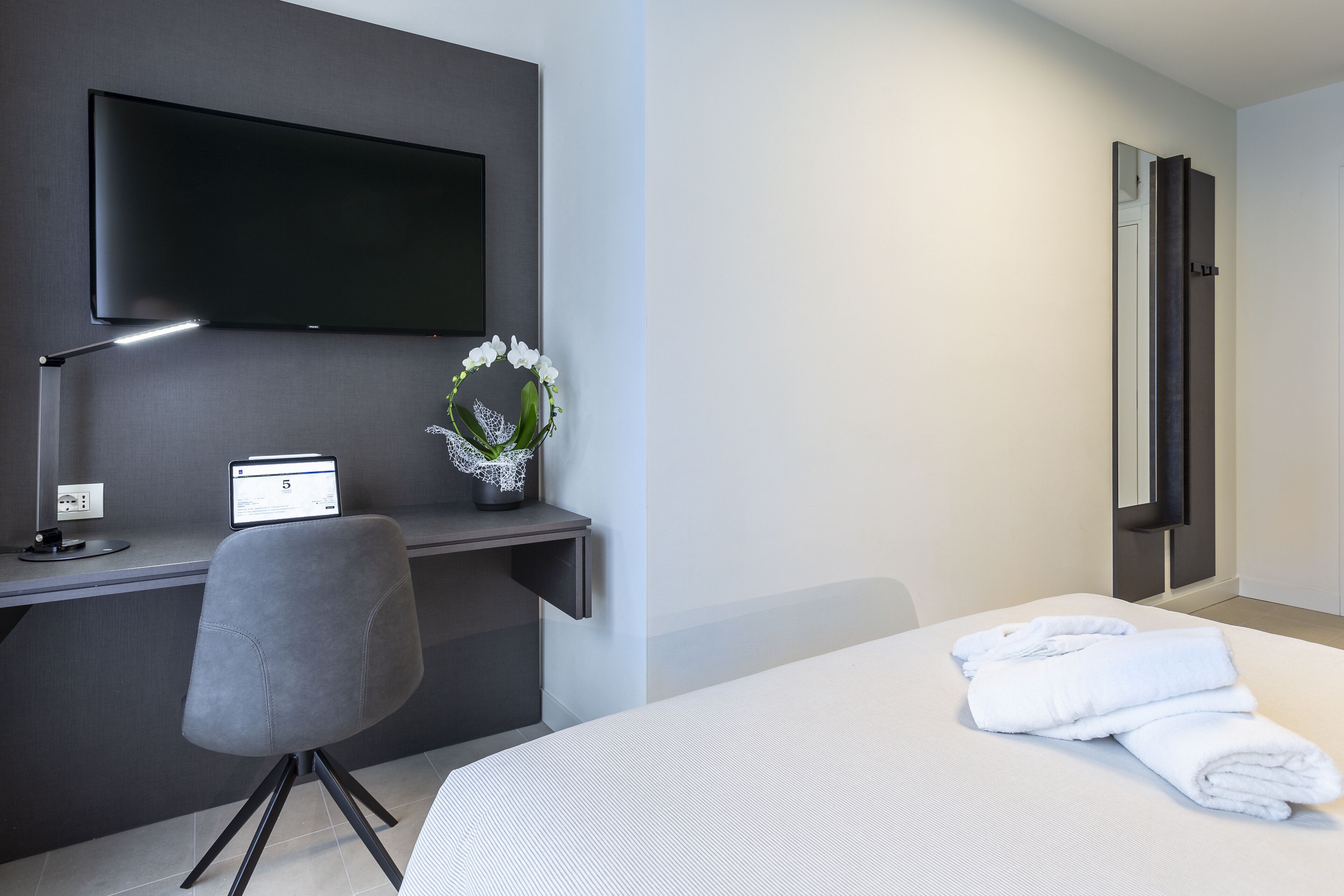 Een hotelkamer met een bed, een bureau met een computer, een televisie en een bloevas.