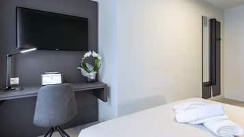 Een hotelkamer met een bed, een bureau met een computer, een televisie en een bloevas.