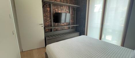 A bedroom with a bed, a wardrobe, a TV mounted on a wall, and a window with curtains.
