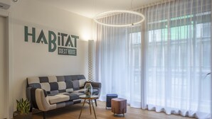 A modern living room with a checkered sofa, a round table, and a potted plant. A sign on the wall reads "HABITAT GUEST HOUSE." - Habitat Guest House (Trento)