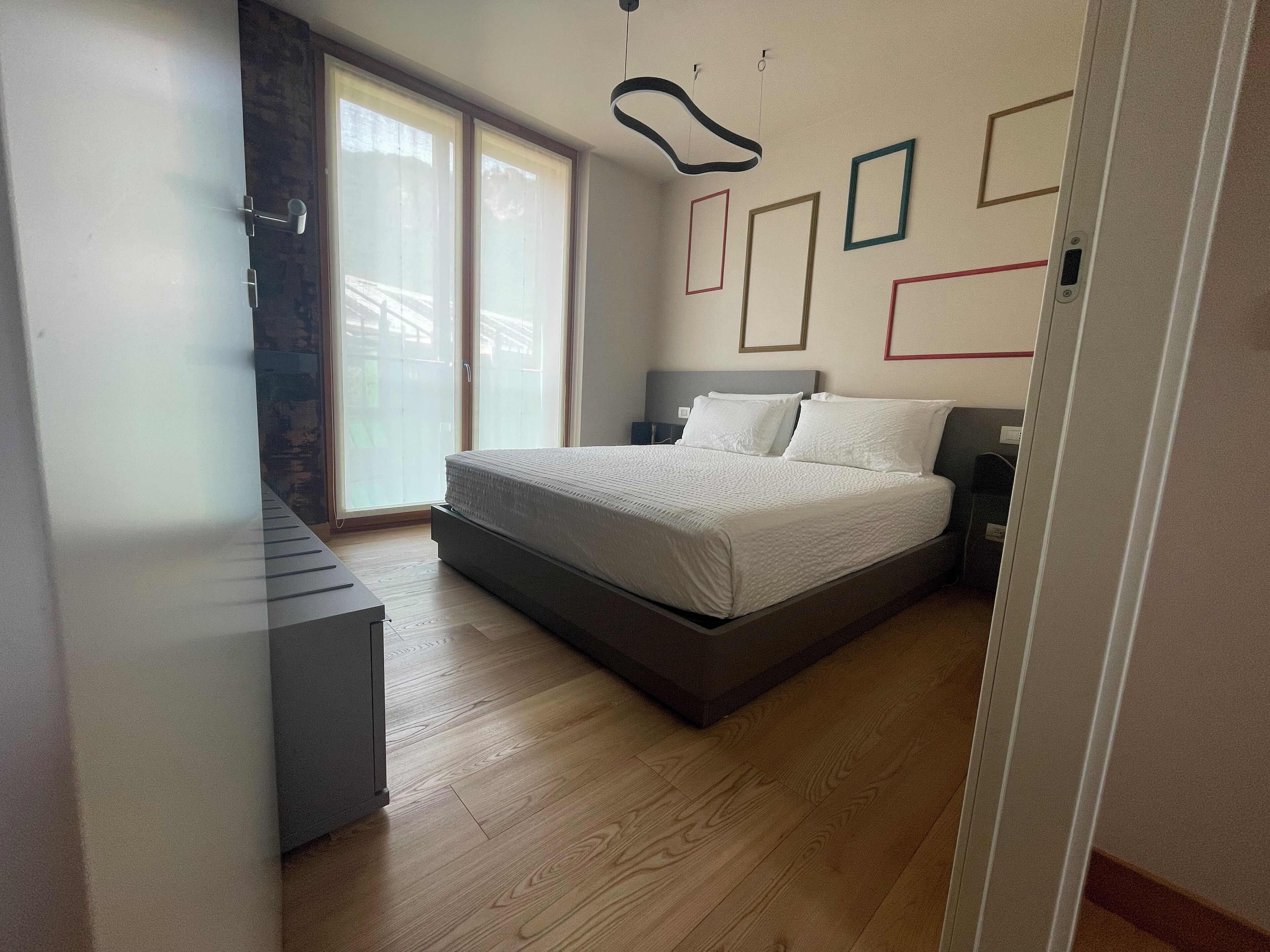 Ein modernes Schlafzimmer mit einem großen Bett, einem Schreibtisch und einer Glastür, die auf einen Balkon führt.