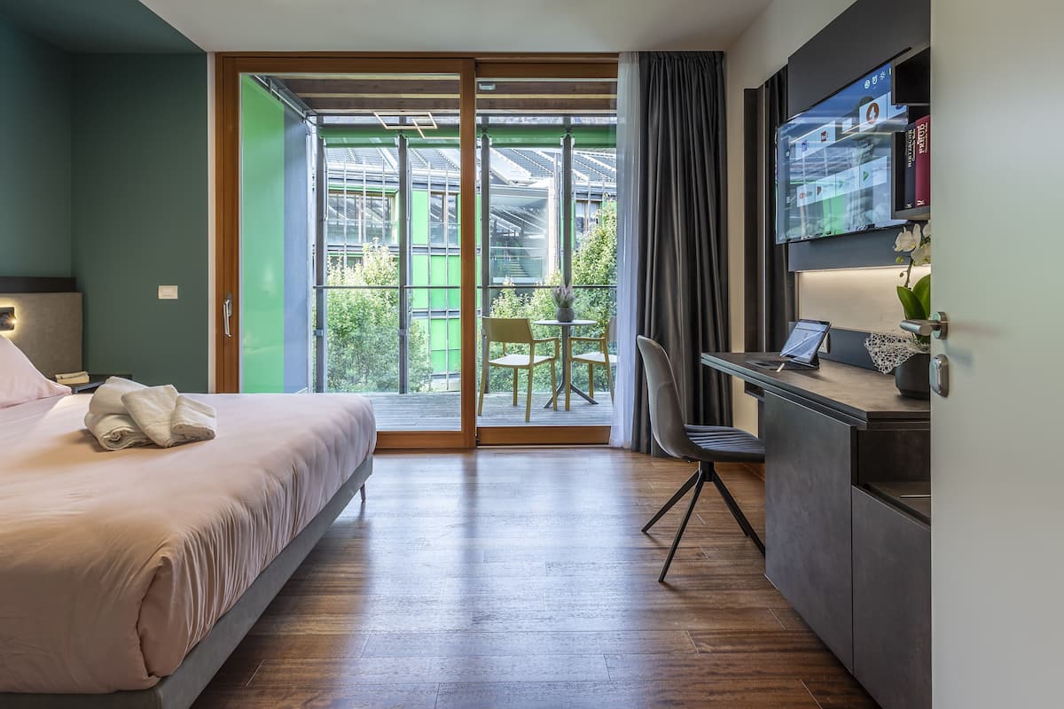 Een moderne hotelkamer met een bed, bureau en grote schuifdeuren naar een balkon.