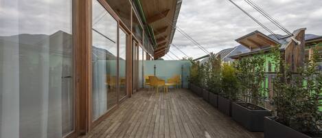 Una terraza de madera con un muro de cristal y un muro verde al fondo.