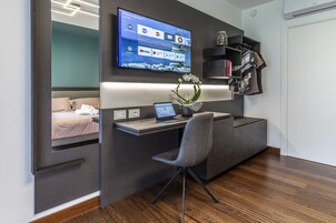A modern bedroom with a built-in desk, a flat-screen TV, and a bed with a view of the city.