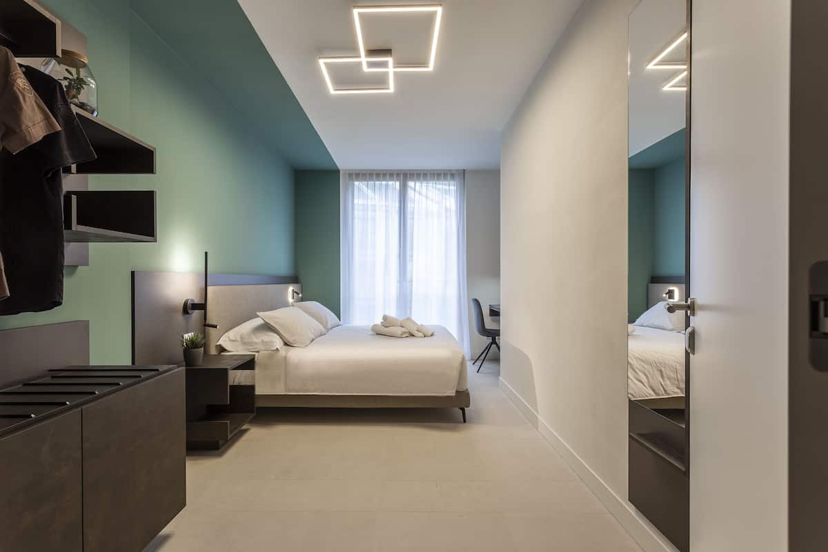 Een moderne hotelkamer met een bed, nachtkastjes, een bureau en een grote spiegel.