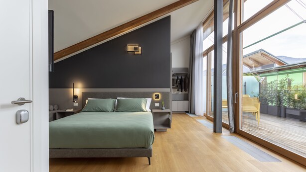 A modern bedroom with a large bed, wooden flooring, a skylight, and a view of the outdoors. - Habitat Guest House (Trento)