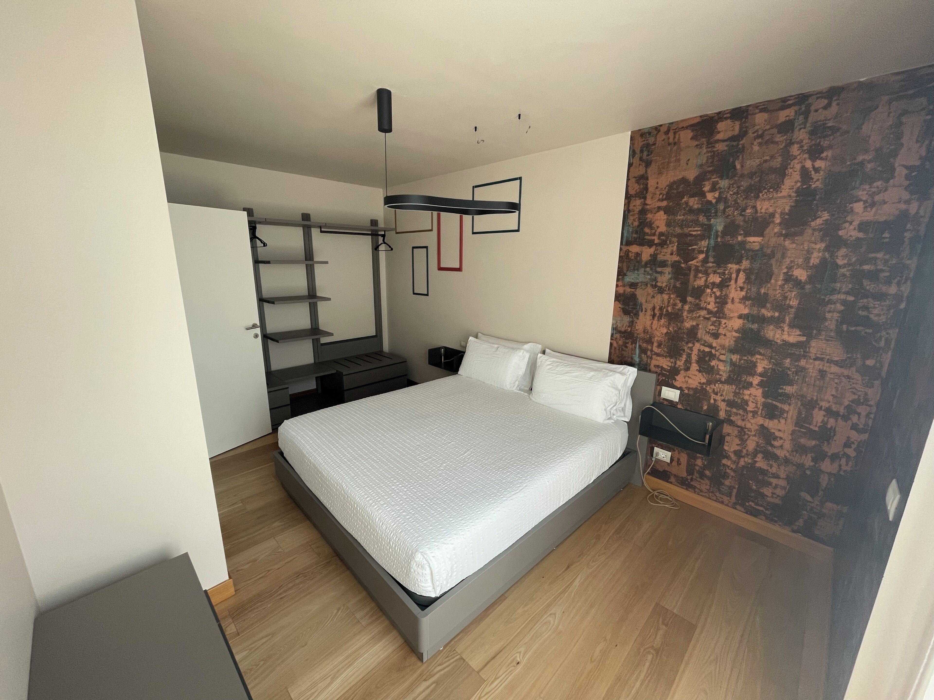 A modern bedroom with a bed, a desk, and a wardrobe.