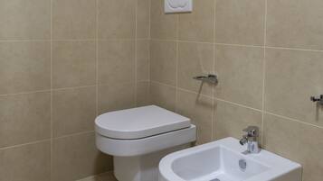 Un baño con azulejos color beige, un inodoro blanco y un bidé blanco.