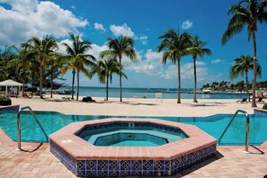 A pool area with a hot tub, palm trees, and a beach view.