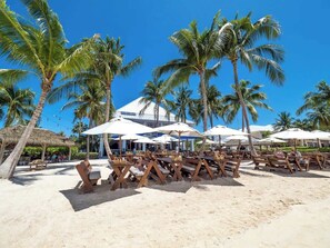 A beachside restaurant with outdoor seating, palm trees, and umbrellas. - Beachfront Crystal Kai 2BR -- Pool, Kayaks & Beach (Cayman Kai)